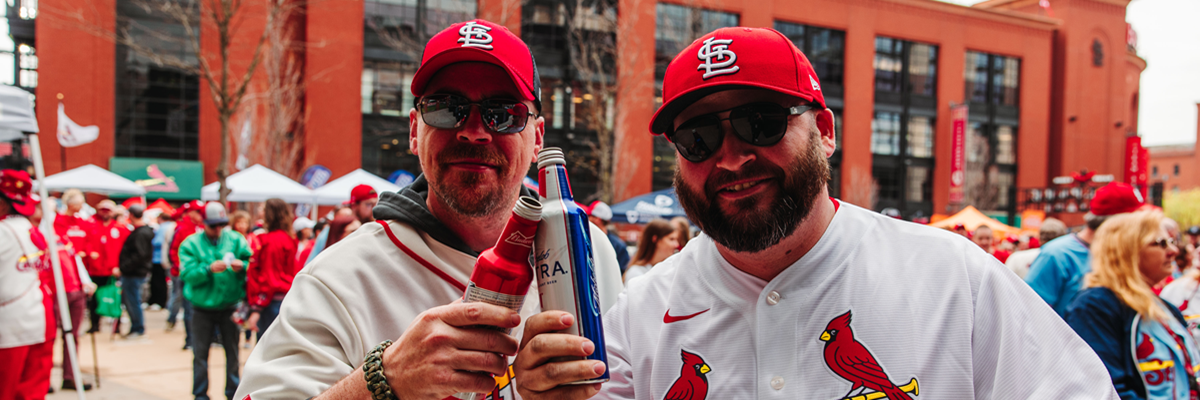 Two male Cardinals fans wearing baseball caps and jerseys toasting beers.